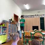 Chłopak z Zespołu Podlesiaki wypowiada się w stronę dzieci siedzących na dywanie. 